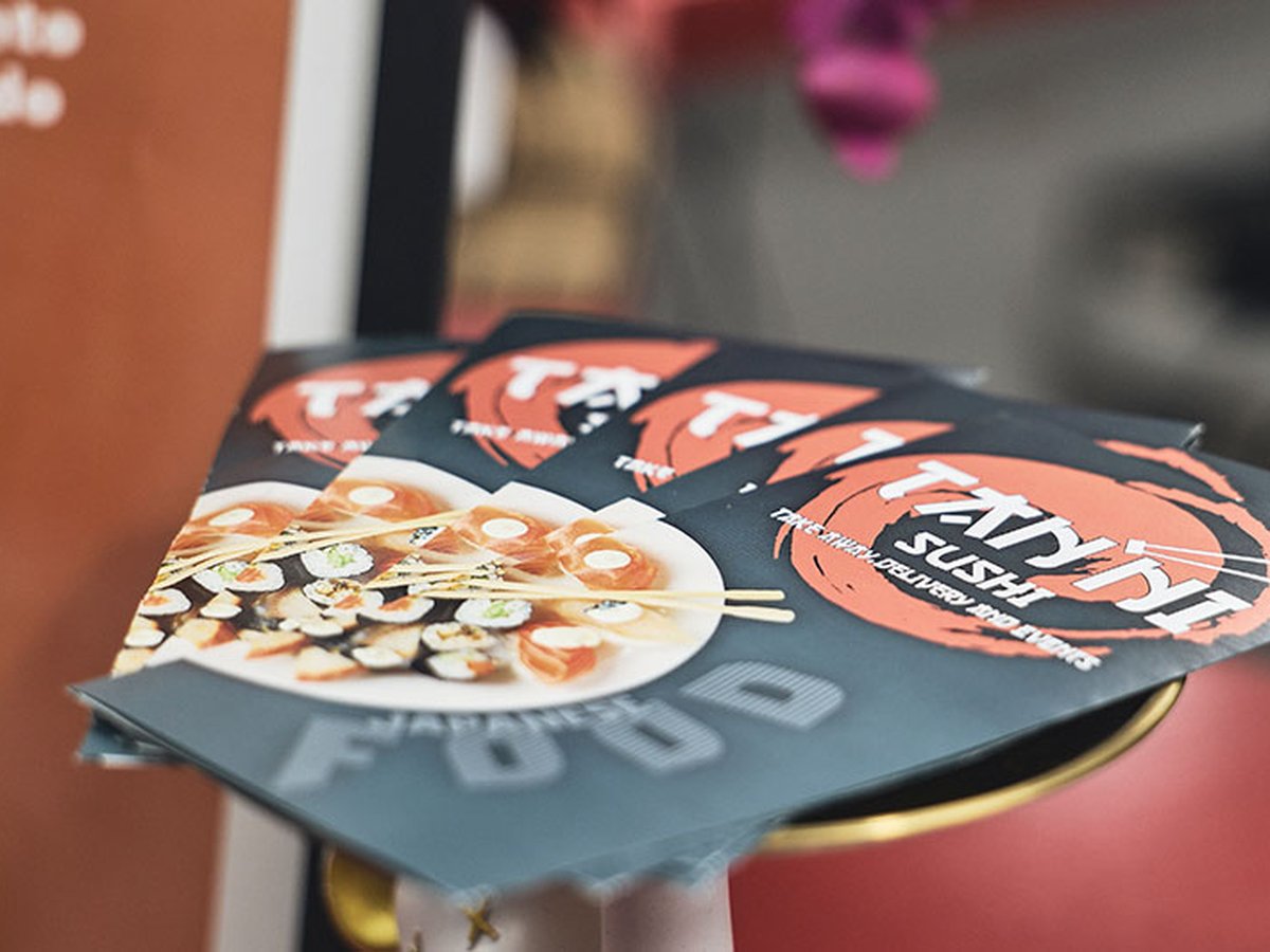 Cartas y flyer de Tanni Sushi sobre un plato de sushi variado